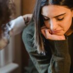 Empathy - Crop woman tapping shoulder and comforting upset female friend while sitting at home together