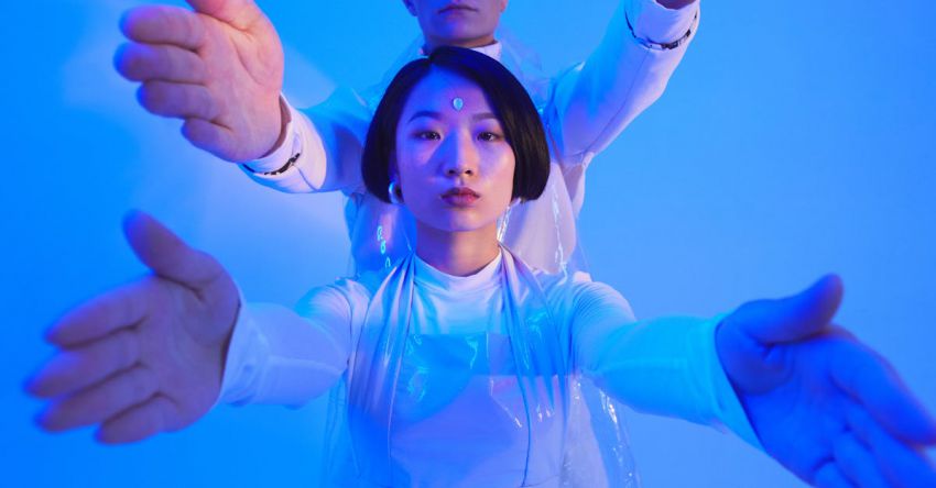 Automation - Young Man and Woman in Futuristic Outfits Standing in Studio with Blue Lighting and Holding Their Arms Up